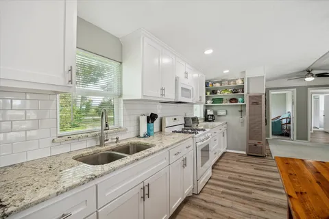 a kitchen with granite countertop a sink stainless steel appliances white cabinets and wooden floor