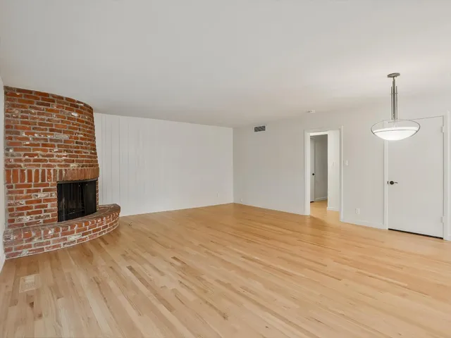 a view of an empty room with wooden floor and a fireplace