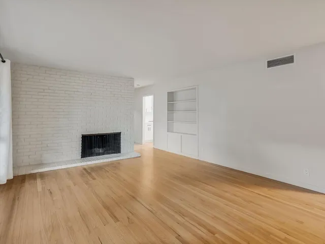 a view of an empty room with wooden floor fireplace and a window