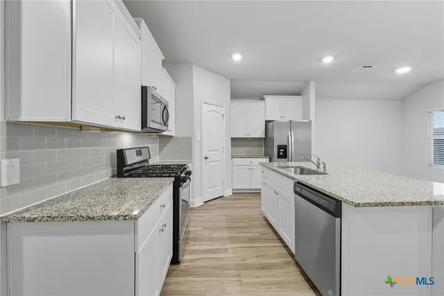 a kitchen with stainless steel appliances granite countertop white cabinets and a stove top oven