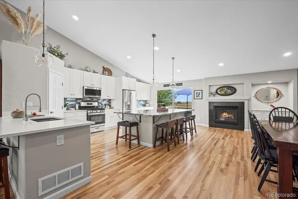 a open kitchen with stainless steel appliances granite countertop a stove top oven a sink dishwasher a dining table and chairs with wooden floor