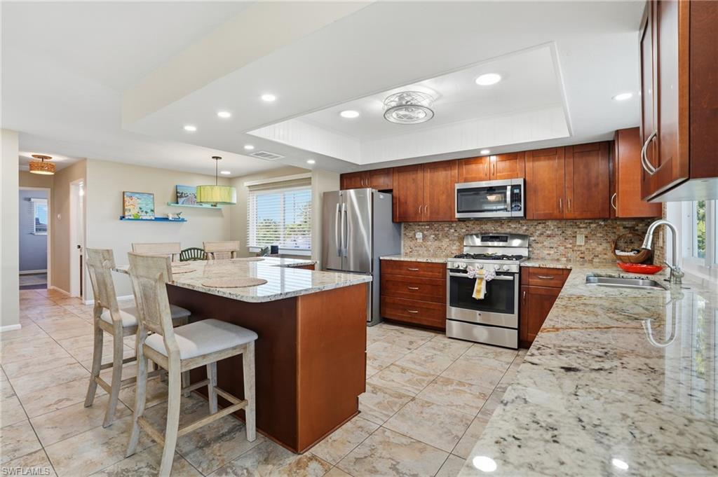 170 Redfish Road Fort Myers Beach, FL 33931 - Photo 11 of 48 a kitchen with stainless steel appliances kitchen island granite countertop a sink a stove a dining table and chairs
