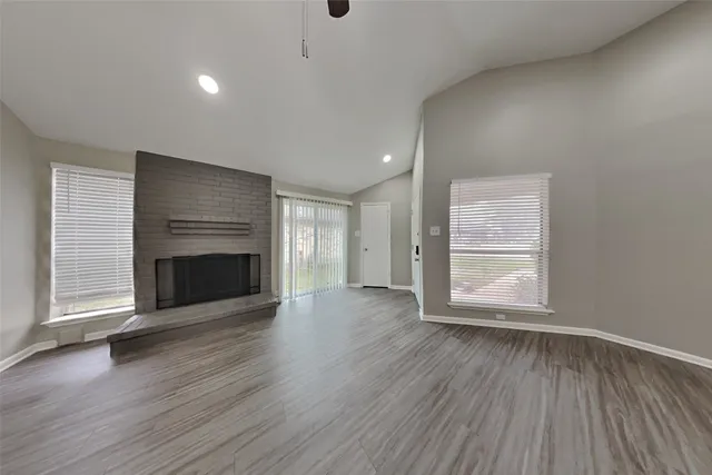 an empty room with wooden floor fireplace and windows