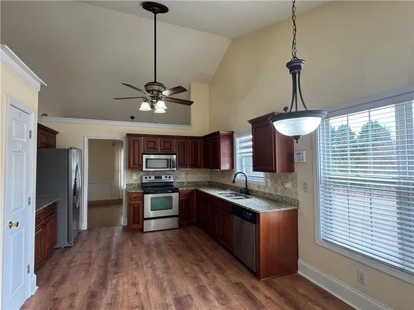 a kitchen with stainless steel appliances granite countertop a refrigerator a sink dishwasher a stove and a dining table with wooden floor
