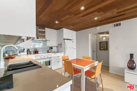 a room with stainless steel appliances kitchen island granite countertop a dining table chairs and a refrigerator