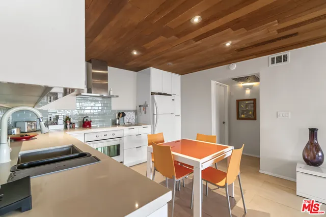 a room with stainless steel appliances kitchen island granite countertop a dining table chairs and a refrigerator