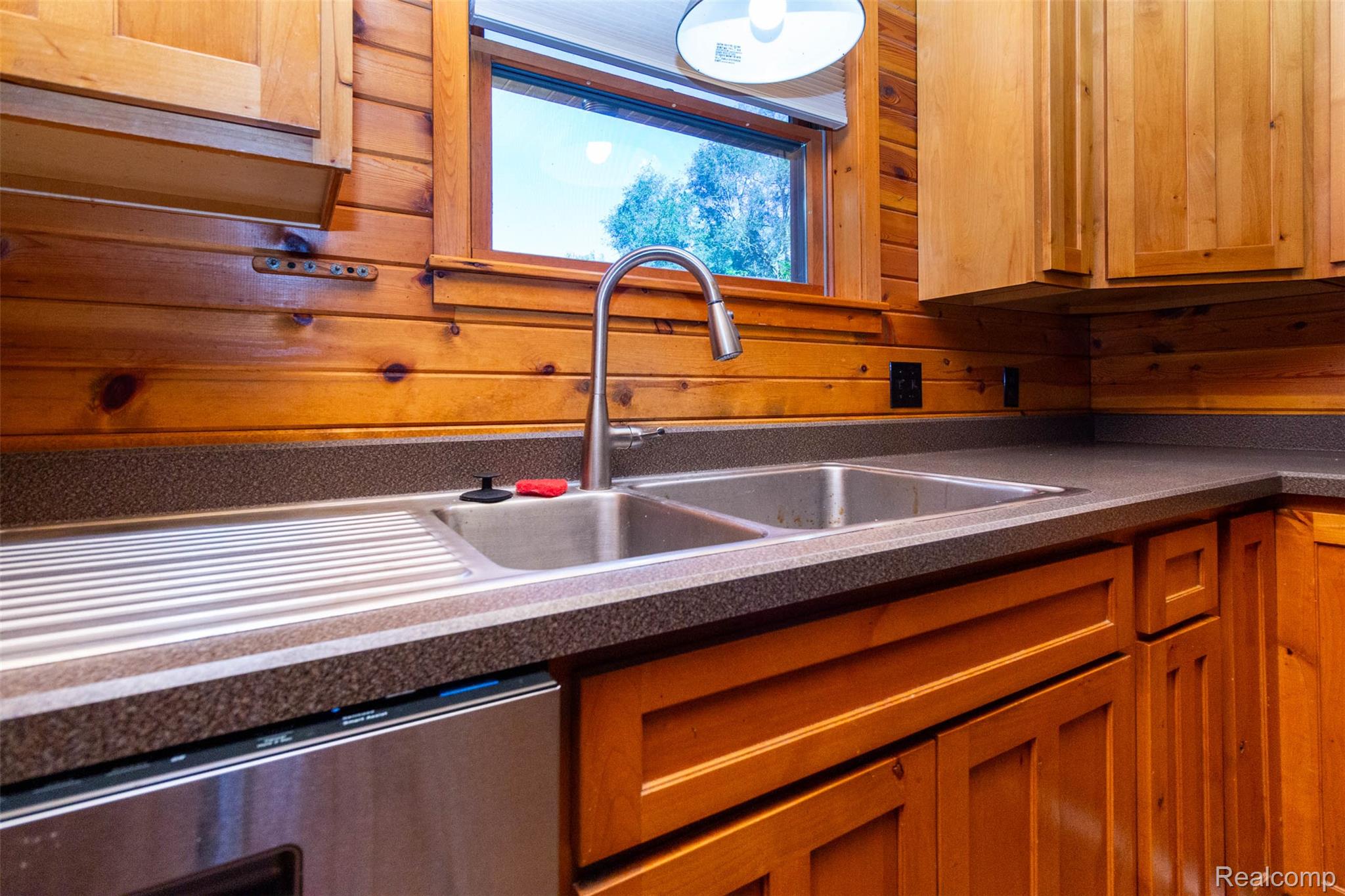 14044 Ridgemont Drive Gregory, MI 48137 - Photo 12 of 33 Wood-paneled wall, dual basin stainless steel sink with integrated drainboard, gooseneck faucet, light wood cabinetry, and dark countertops