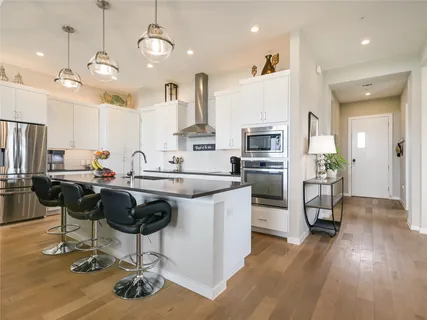 a kitchen with stainless steel appliances granite countertop a refrigerator oven a stove a sink a dining table and chairs with wooden floor