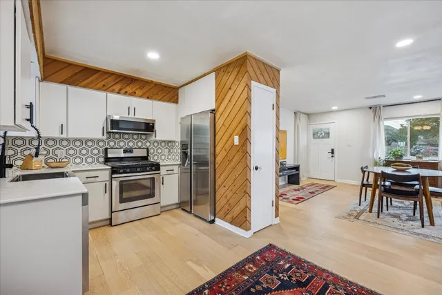 a kitchen with stainless steel appliances granite countertop a stove top oven a refrigerator a dining table and chairs with wooden floor