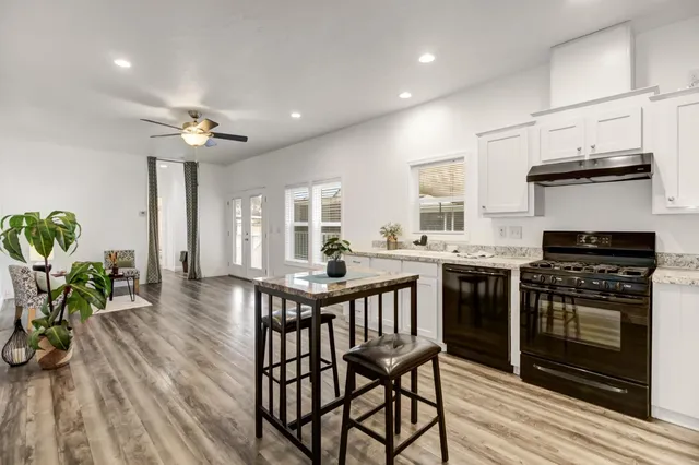 a kitchen with stainless steel appliances a stove a sink dishwasher a dining table and chairs with wooden floor