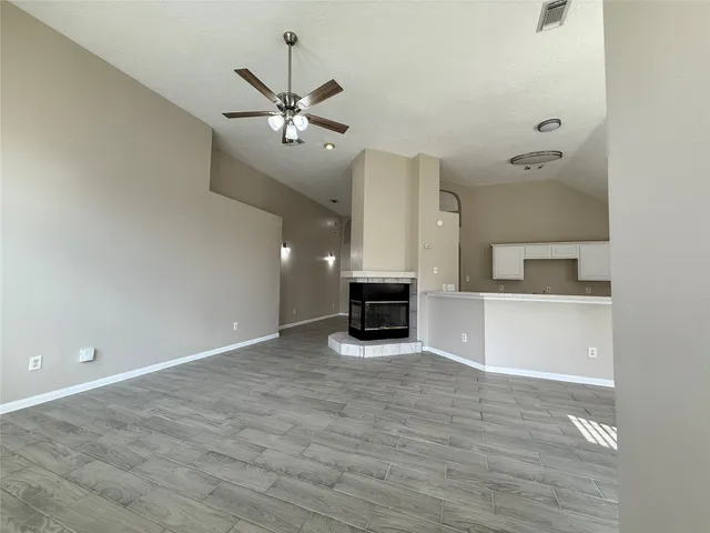 a view of an empty room with a fireplace and a ceiling fan