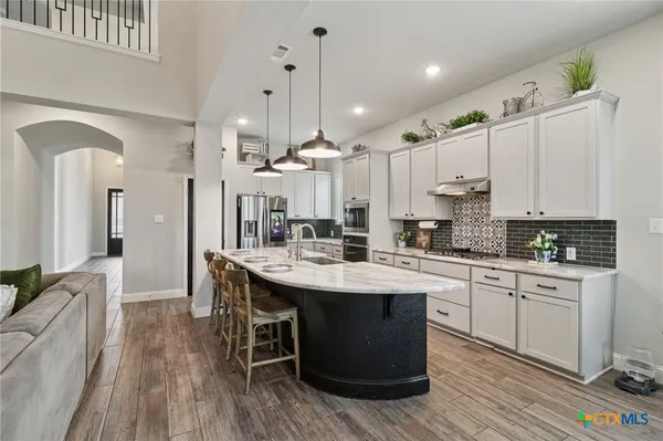 a kitchen with stainless steel appliances granite countertop a sink a stove a refrigerator and island with wooden floor