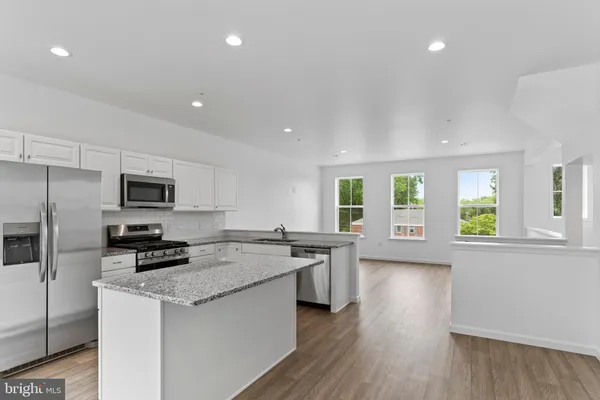 a kitchen with stainless steel appliances granite countertop a stove a sink a refrigerator white cabinets and wooden floor