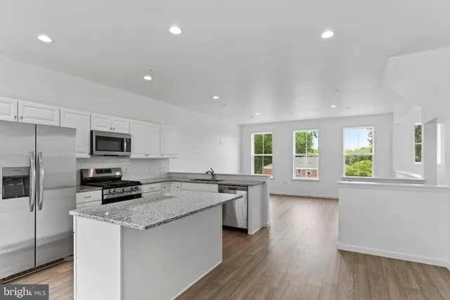 a kitchen with stainless steel appliances granite countertop a stove a sink a refrigerator white cabinets and wooden floor