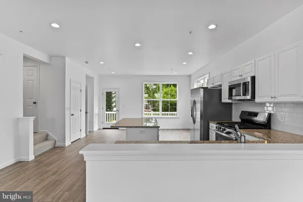 a large white kitchen with stainless steel appliances granite countertop a stove a sink a refrigerator a dining table and chairs with wooden floor
