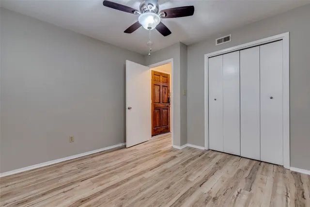 a view of an empty room with wooden floor and a ceiling fan