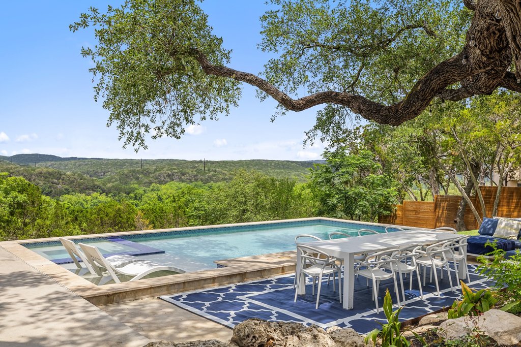 716 North Commons Ford Road Austin, TX 78733 - Photo 2 of 30 Terraced outdoor entertaining area featuring a rectangular pool with an integrated baja shelf and steps, stone coping, and lush surrounding trees