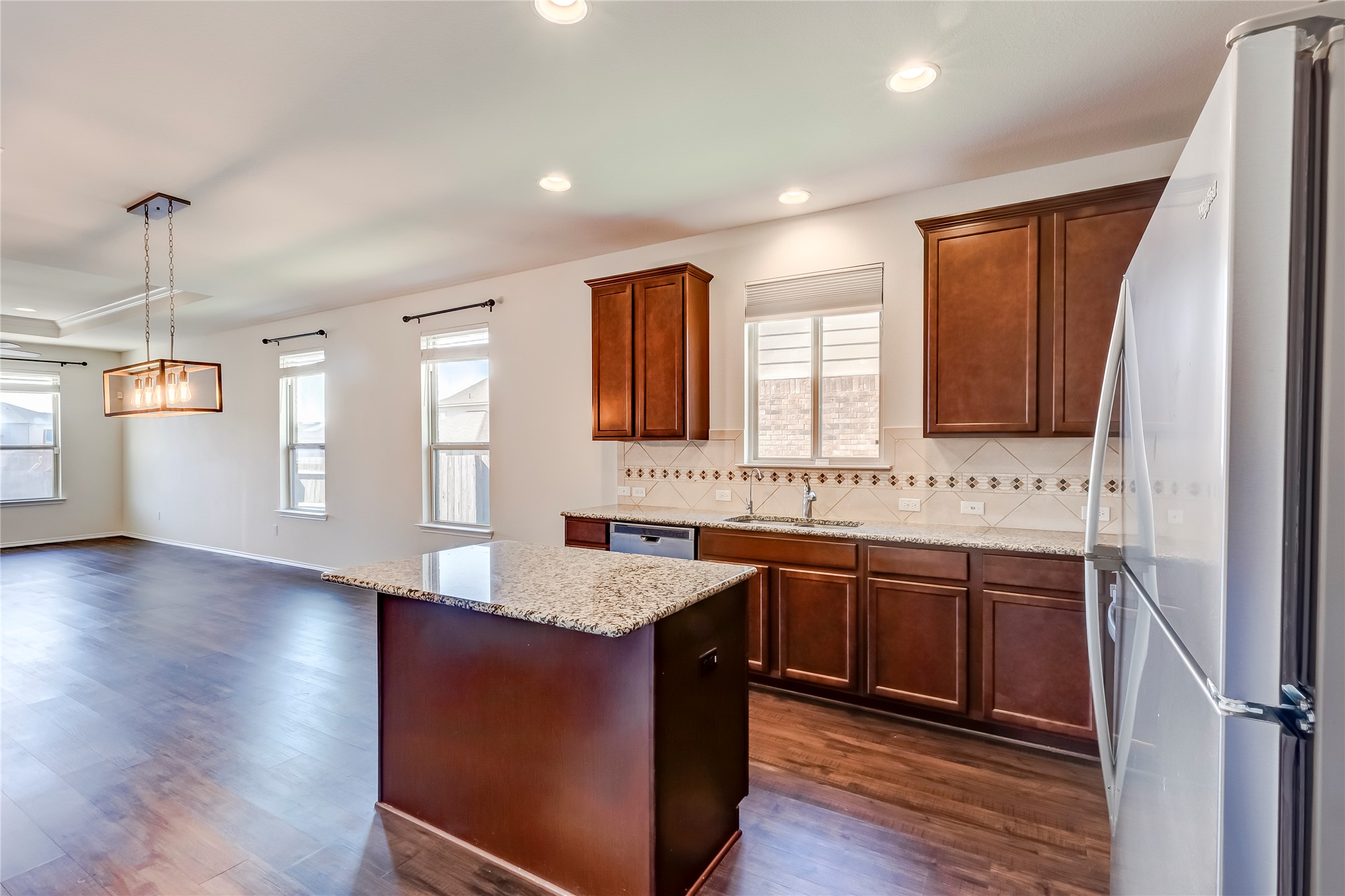11617 Amber Stream Lane Manor, TX 78653 - Photo 10 of 39 Kitchen featuring freestanding refrigerator, light stone countertops, a center island, dark wood-type flooring, and decorative backsplash