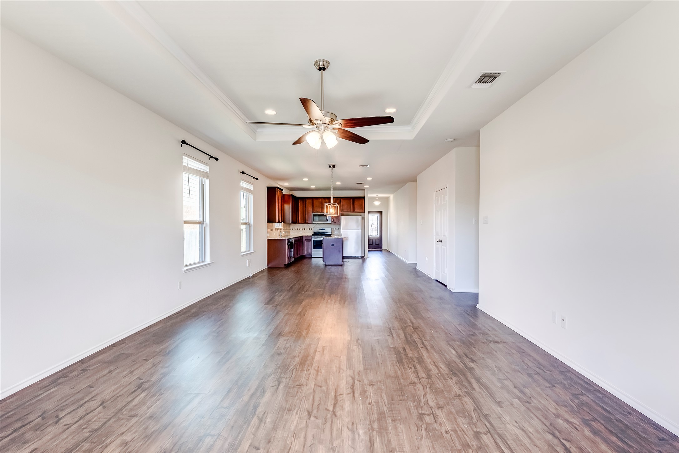 11617 Amber Stream Lane Manor, TX 78653 - Photo 6 of 39 Unfurnished living room with a ceiling fan, a tray ceiling, dark wood-style flooring, recessed lighting, and crown molding