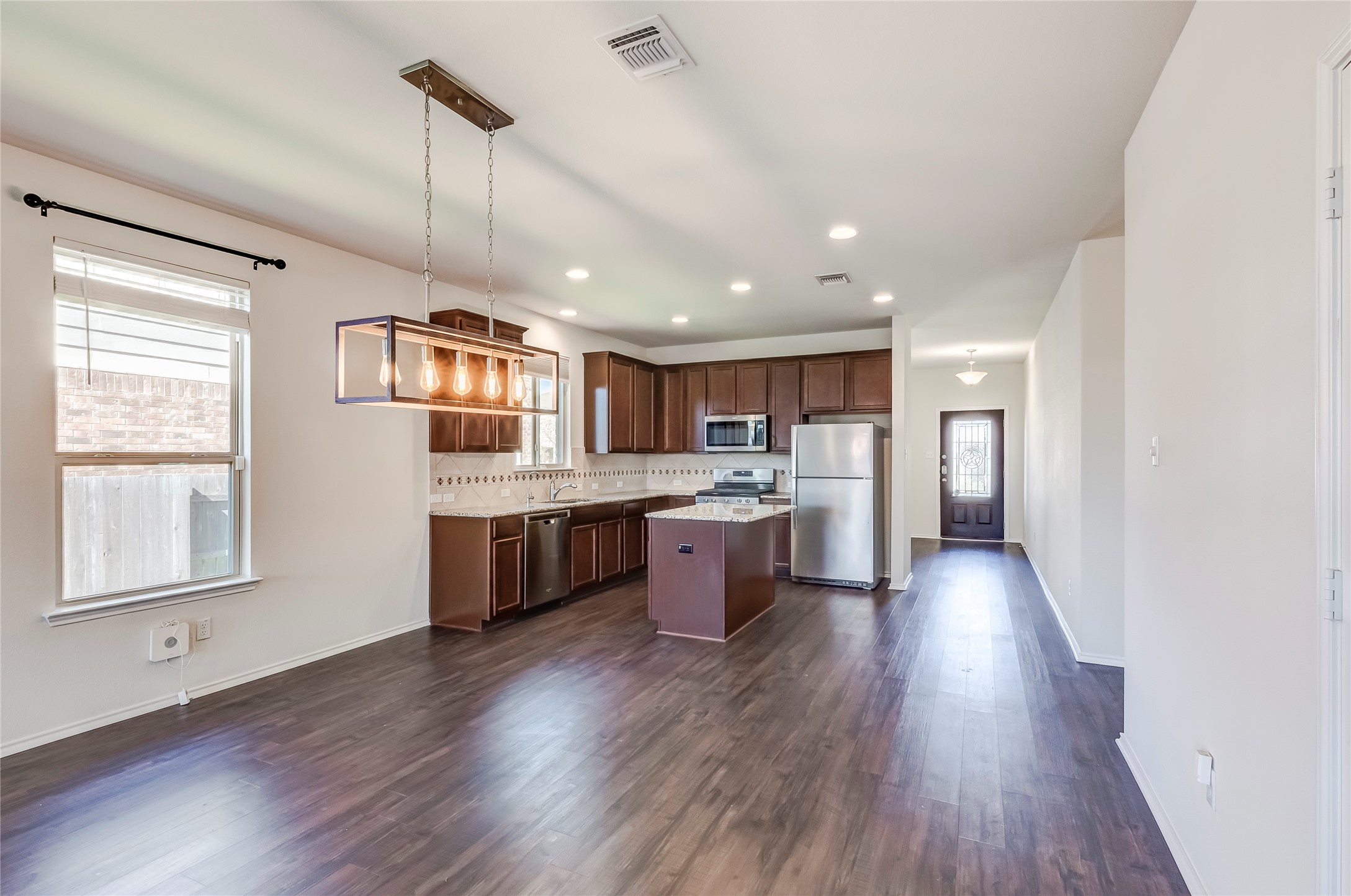 11617 Amber Stream Lane Manor, TX 78653 - Photo 8 of 39 Kitchen with stainless steel appliances, a center island, dark wood-style flooring, decorative light fixtures, and light stone counters
