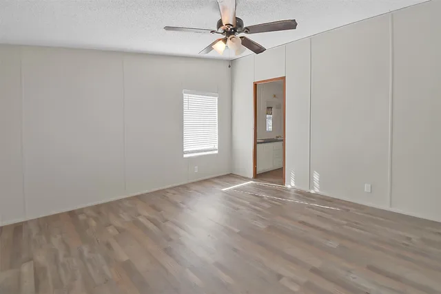 an empty room with wooden floor ceiling fan and windows