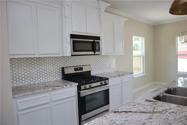 a kitchen with granite countertop white cabinets appliances and a window