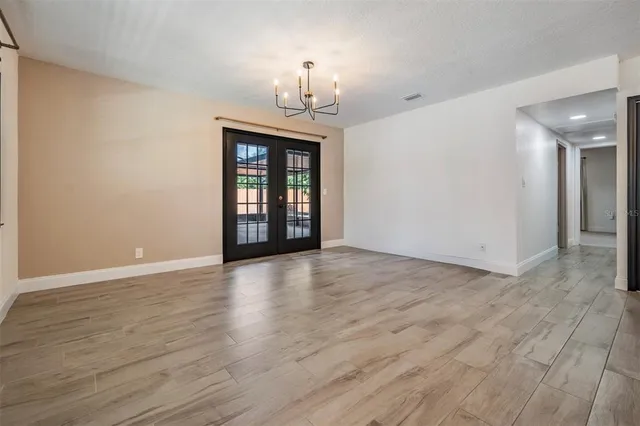 an empty room with wooden floor chandelier and windows