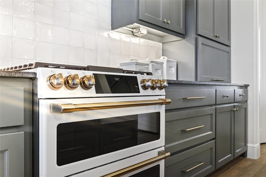 10978 Gregory Road Sanger, TX 76266 - Photo 20 of 40 Contemporary kitchen featuring a white and stainless steel dual wall oven with gold hardware accents, five-burner gas cooktop with matching gold trim, gray shaker-style cabinetry with brushed metal handles, white subway tile backsplash, and wood-finish flooring