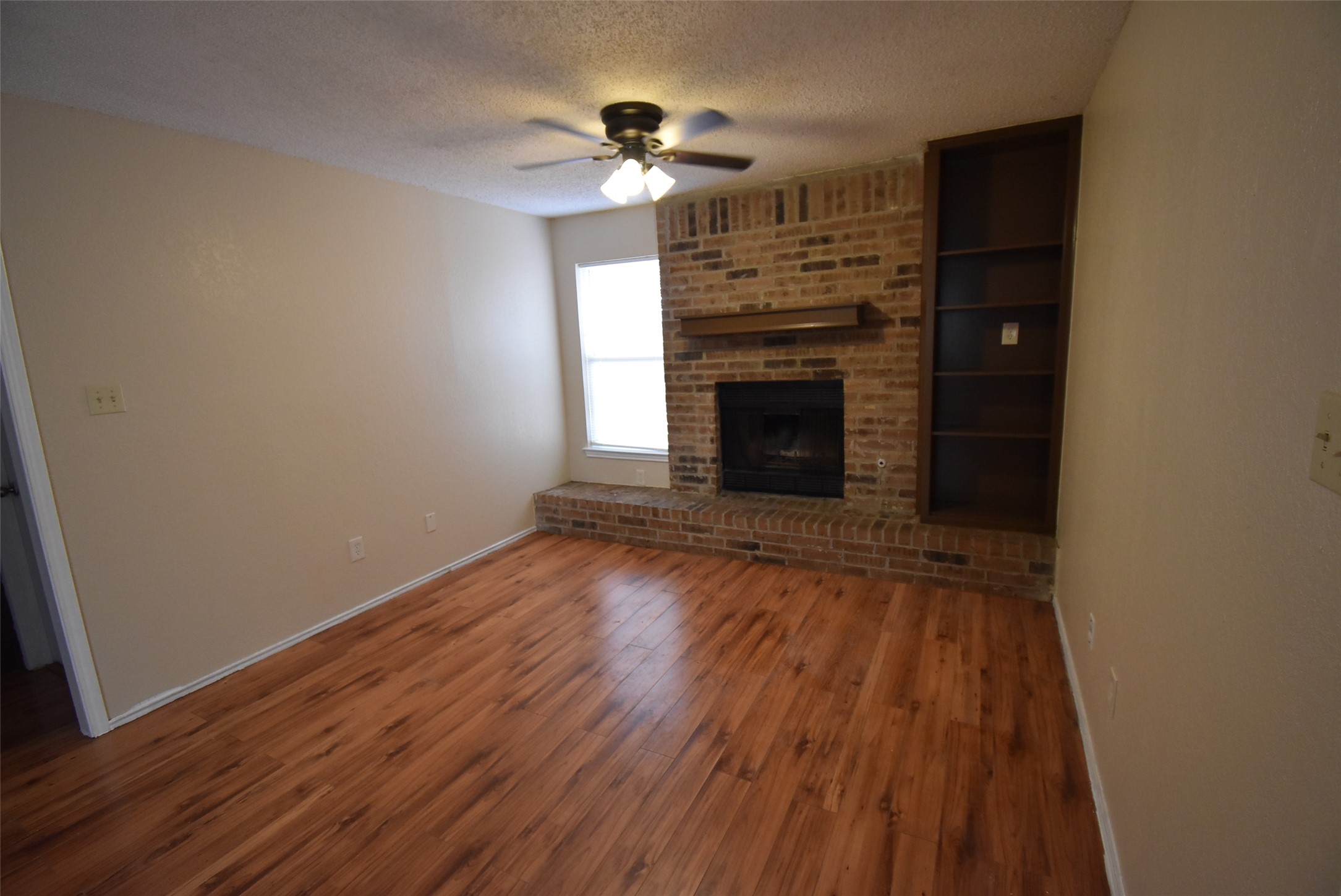 1806 Rawhide Loop Round Rock, TX 78681 - Photo 2 of 23 Unfurnished living room with laminate floors, ceiling fan, textured ceiling, brick fireplace and bookshelves