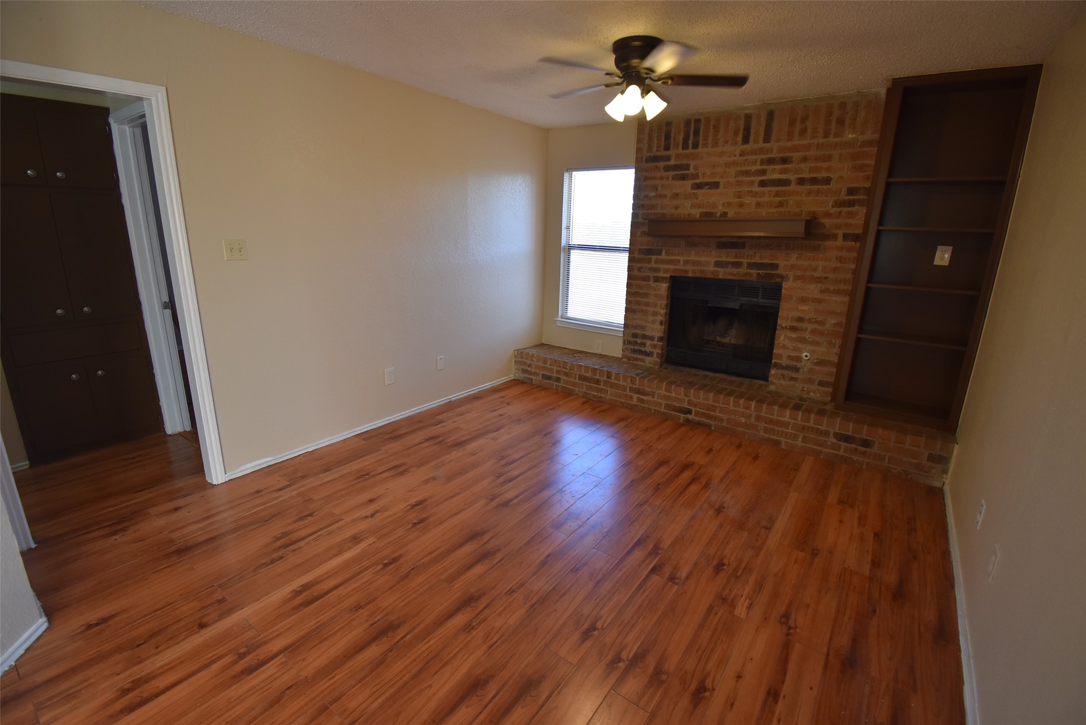 1806 Rawhide Loop Round Rock, TX 78681 - Photo 3 of 23 Unfurnished living room featuring ceiling fan, laminate floors, brick fireplace, and textured ceiling