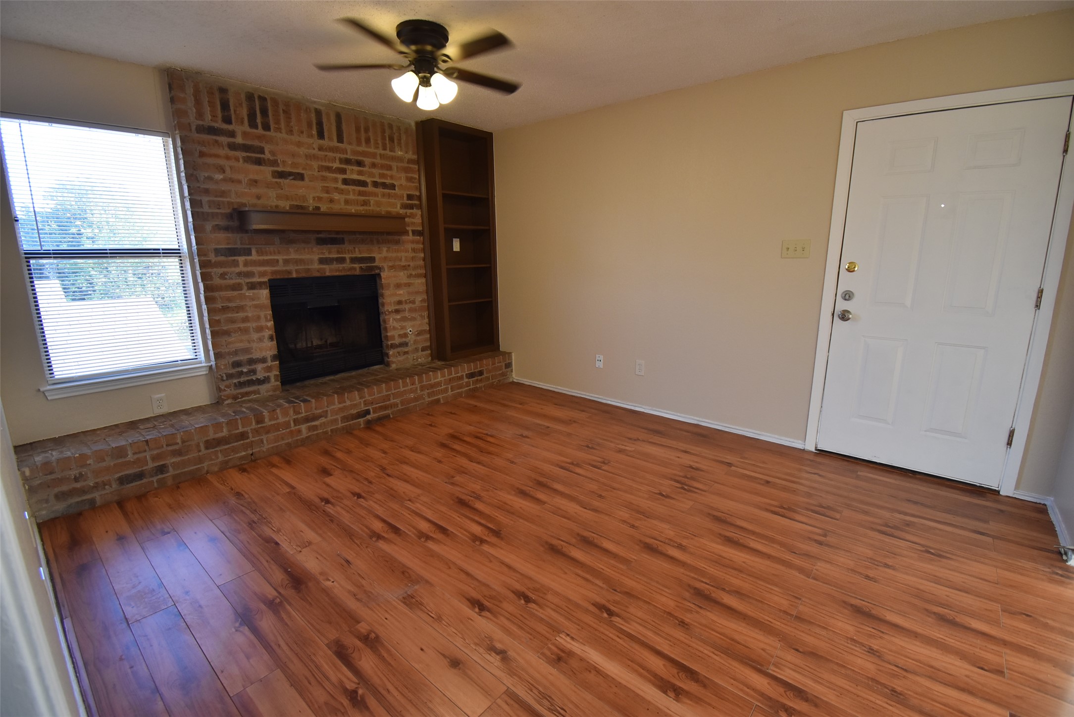 1806 Rawhide Loop Round Rock, TX 78681 - Photo 4 of 23 Unfurnished living room with ceiling fan, laminate flooring, brick fireplace and bookshelves