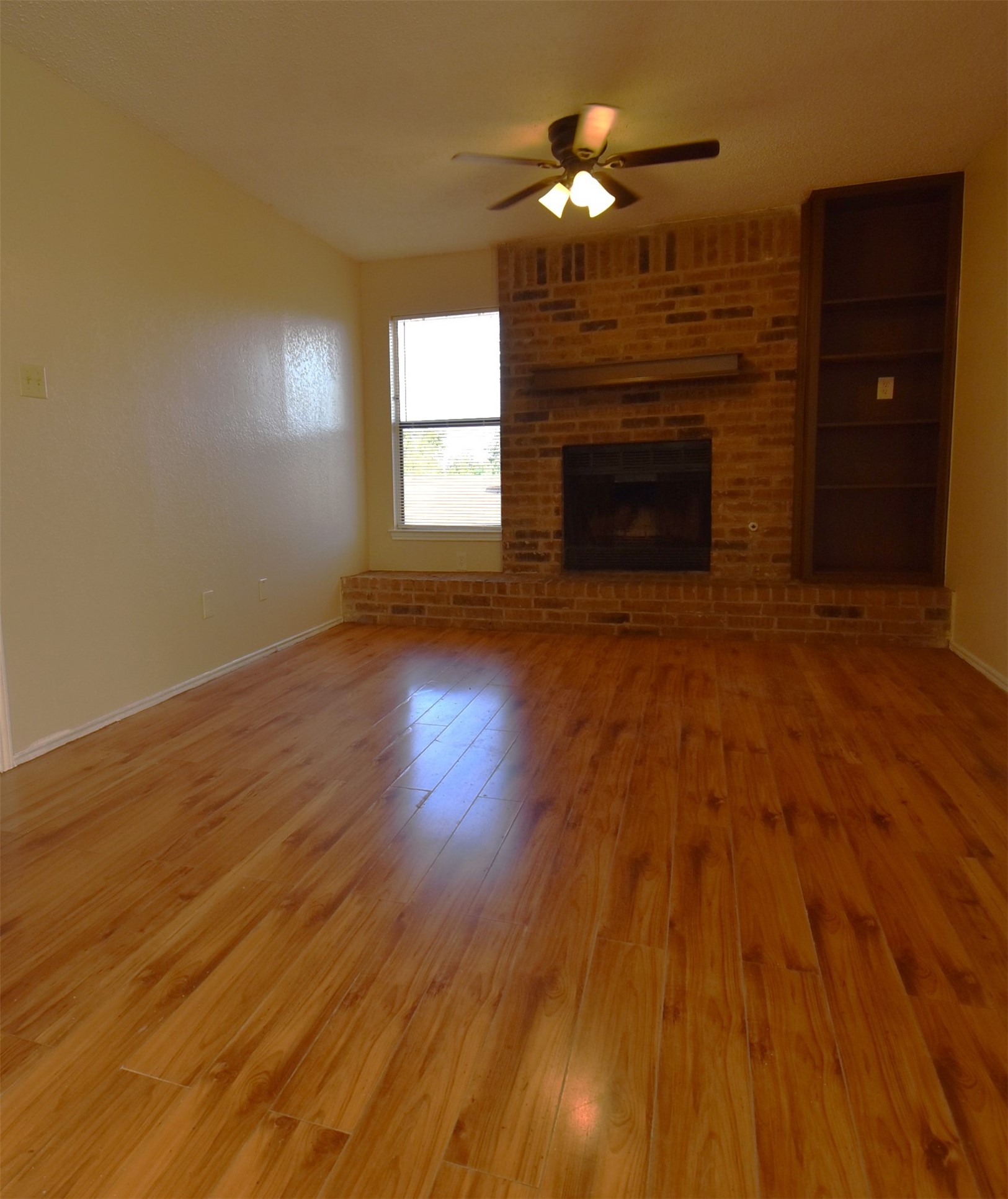 1806 Rawhide Loop Round Rock, TX 78681 - Photo 5 of 23 Unfurnished living room featuring laminate flooring, ceiling fan, brick fireplace and bookshelves