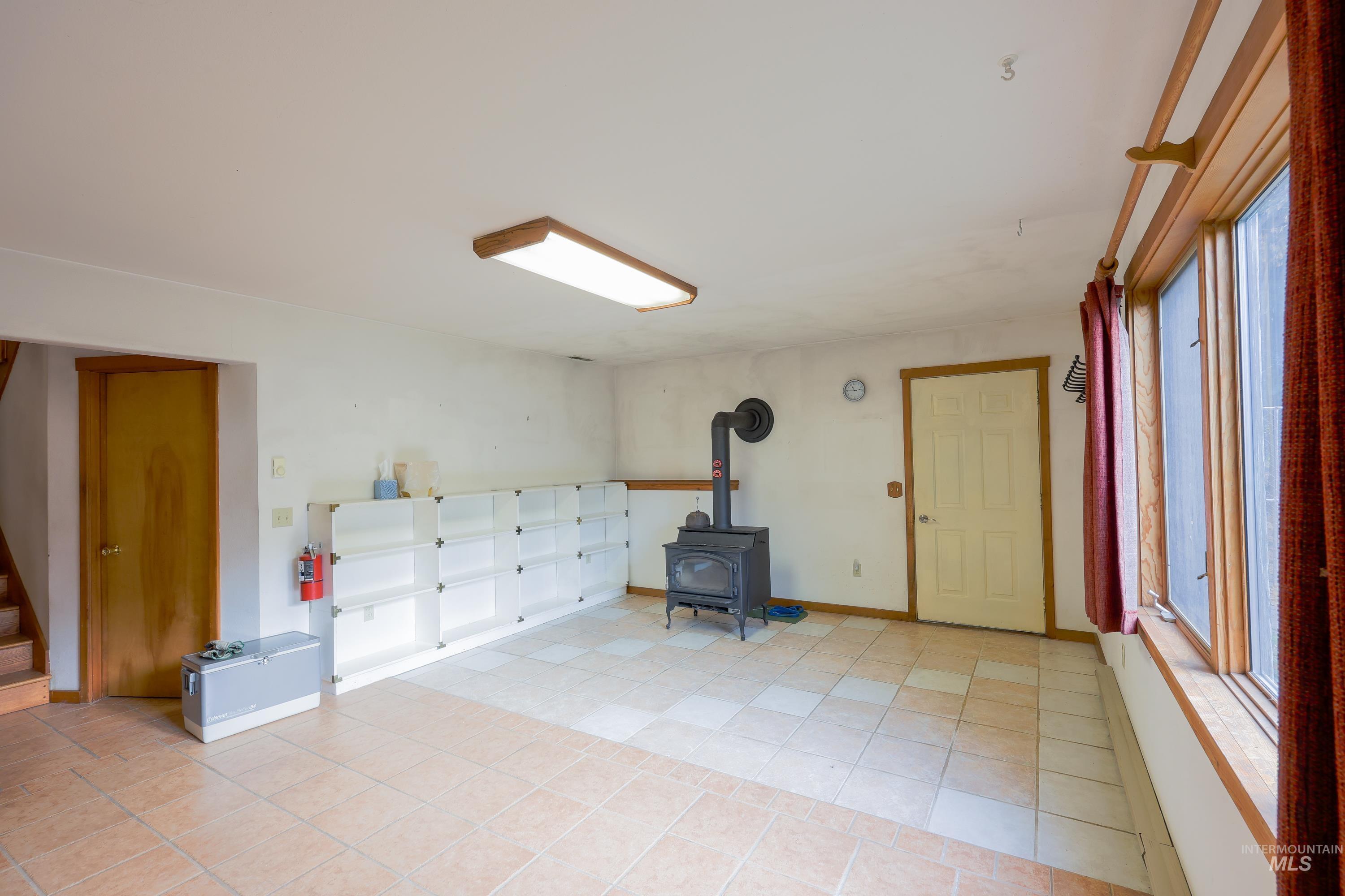 1021 Claypit Road Troy, ID 83871 - Photo 29 of 44 Basement with a wood stove, light tile patterned floors, and stairway