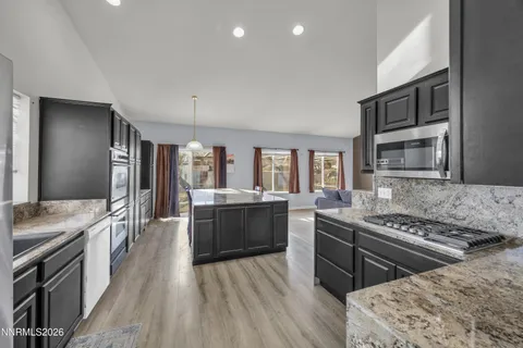 a kitchen with stainless steel appliances granite countertop a stove top oven a sink dishwasher a dining table and chairs with wooden floor