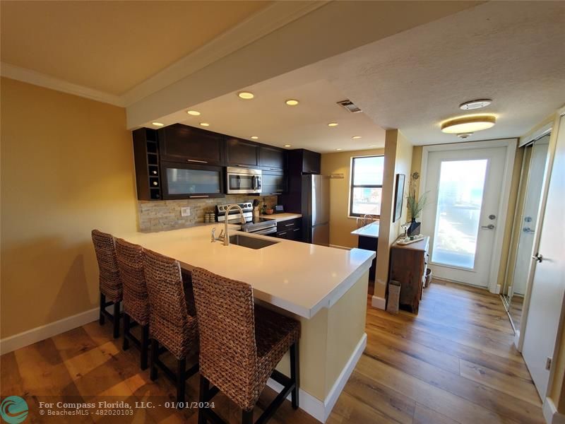 a living room with stainless steel appliances a dining table wooden floor and a view of kitchen