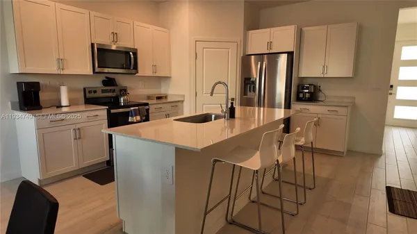 a kitchen with stainless steel appliances a stove a sink a microwave a refrigerator a stove and white cabinets