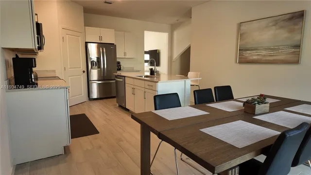 a open kitchen with stainless steel appliances kitchen island granite countertop a refrigerator a stove a sink dishwasher a dining table and chairs with wooden floor