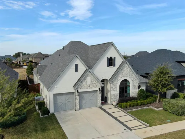 a view of a white house with a yard plants and large tree