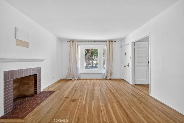 a view of an empty room with wooden floor fireplace and a window