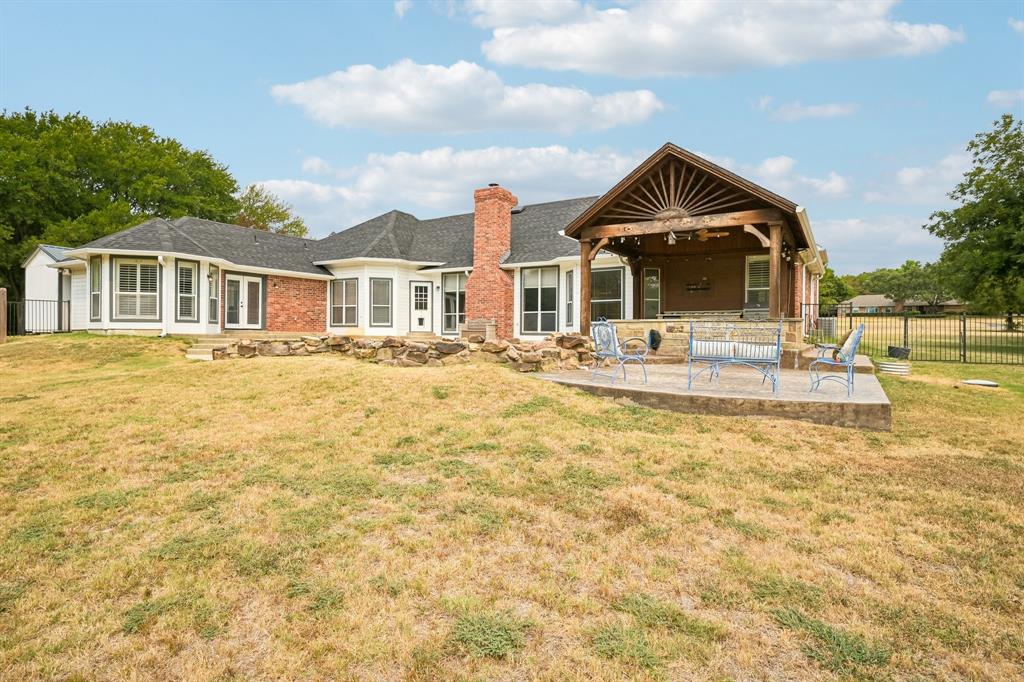 1380 Meandro Ria Lane Fairview, TX 75069 - Photo 33 of 39 Expansive backyard featuring a covered patio with a wood-beamed ceiling, a brick exterior, multiple large windows, and a black wrought-iron fence