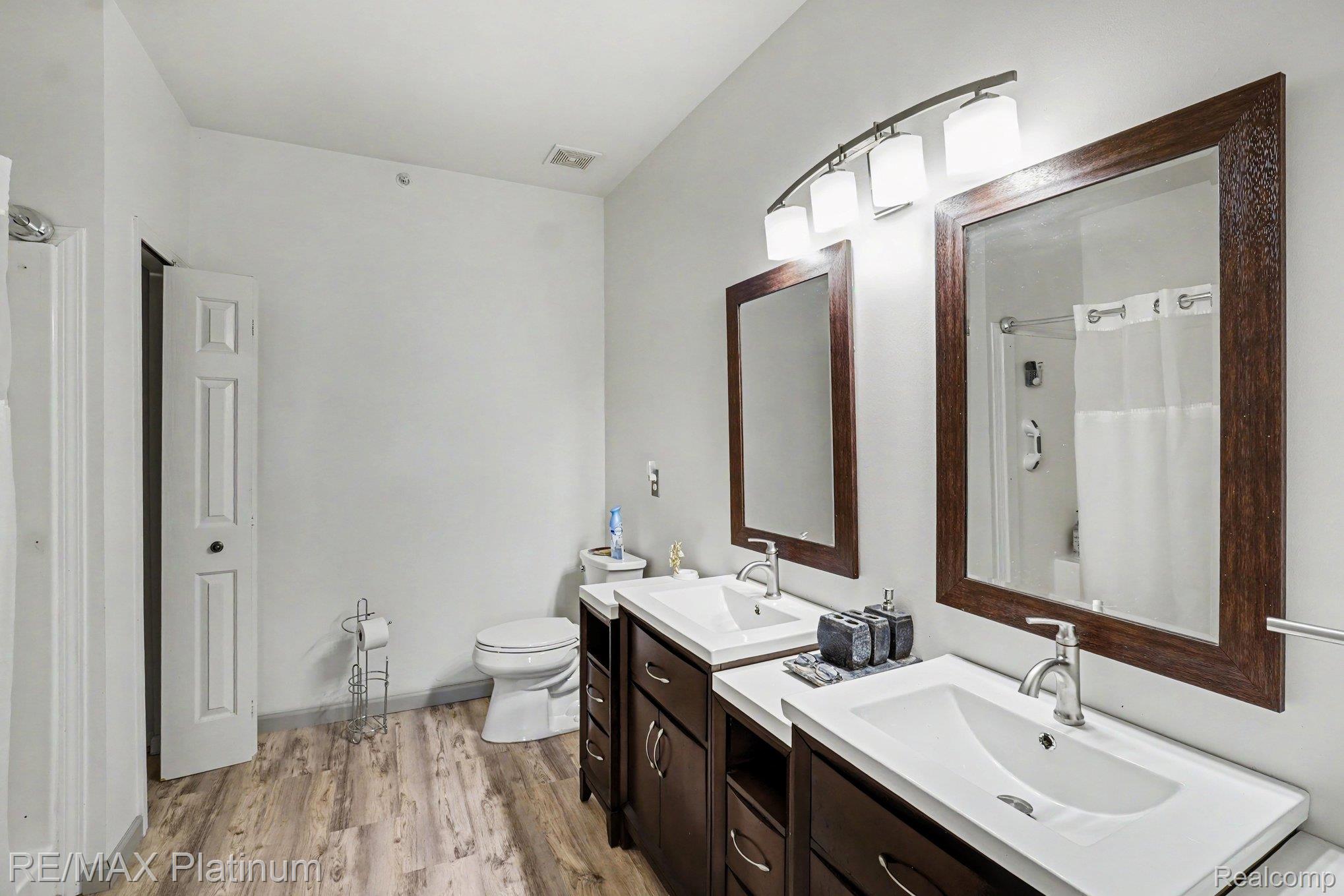 10217 Crossview Trail Howell, MI 48855 - Photo 22 of 26 Bathroom featuring a dual vanity with white countertops, wood-finish flooring, and two framed mirrors