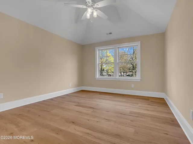 an empty room with wooden floor chandelier fan and windows