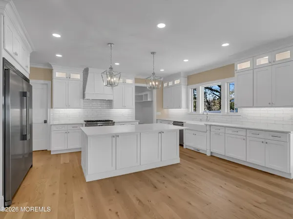 a large kitchen with kitchen island a sink dishwasher a refrigerator and white cabinets with wooden floor