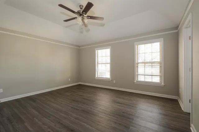 an empty room with wooden floor fan and windows