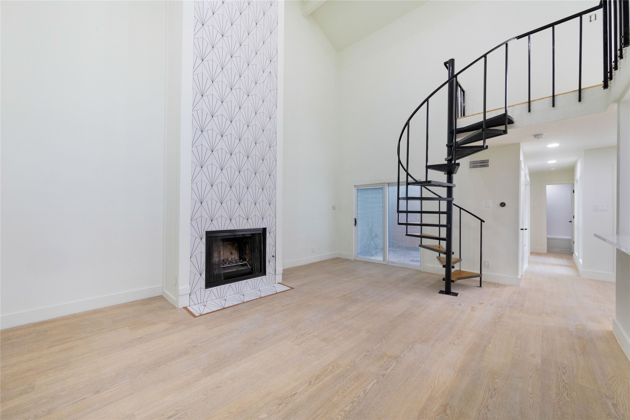 A striking fireplace with a unique tiled design anchors this generously proportioned living area, complemented by a sleek spiral staircase leading to an upper level.