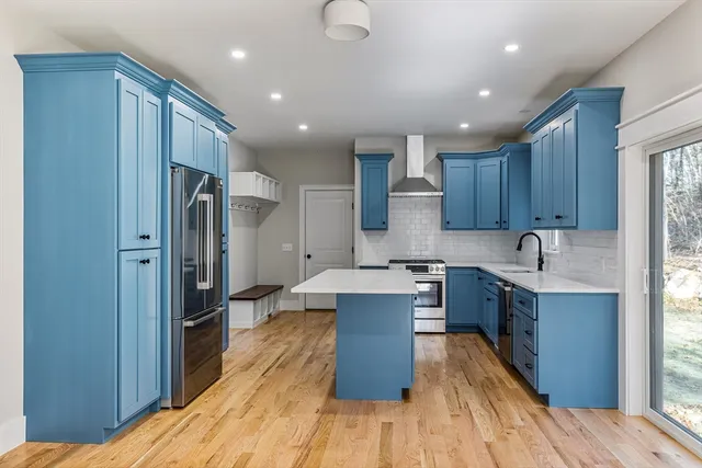 a kitchen with stainless steel appliances granite countertop a refrigerator a sink dishwasher a stove and white countertops with wooden floor