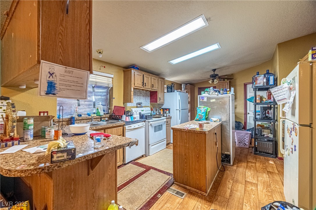 4231 West Wilson Road Pahrump, NV 89048 - Photo 4 of 15 Kitchen with light wood-style flooring, a peninsula, white appliances, ceiling fan, and a center island