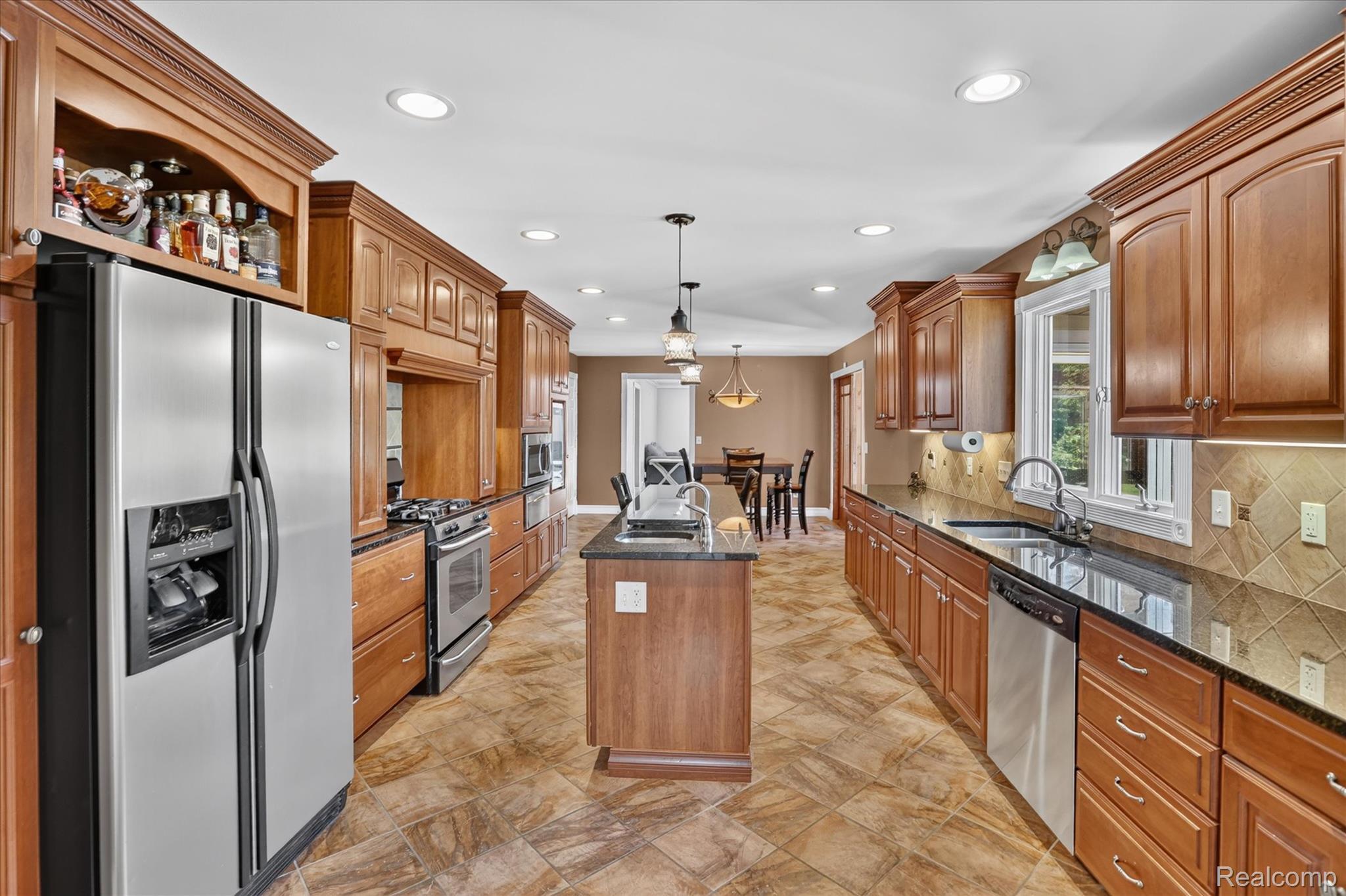 7186 East River Road Flushing, MI 48433 - Photo 8 of 47 Expansive kitchen featuring wood cabinetry, stainless steel appliances, a center island with pendant lighting, stone countertops, and tile flooring