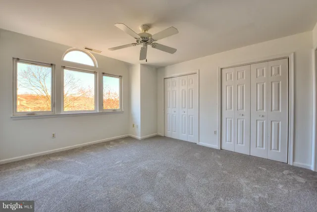 an empty room with chandelier fan and windows