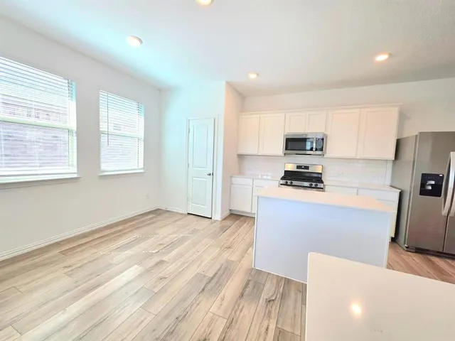 a kitchen with stainless steel appliances a stove a refrigerator a sink and white cabinets with wooden floor